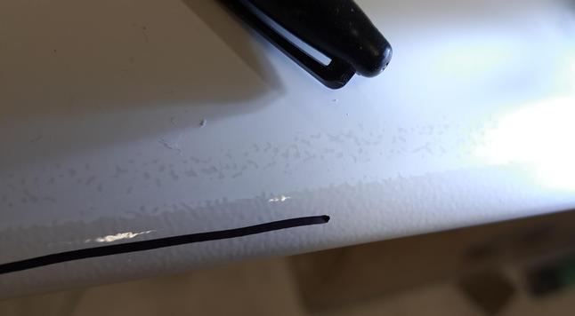 Closeup view of the leading edge of the glider wing. The black cap of a Sharpie marker is there to provide scale. A flashlight, just outside the right side of the frame, is shining on the painted surface at a very low angle. The unsanded surface shows orange peel. A black marker line has been drawn on the unsanded portion to serve as a progress mark during tomorrow's sanding.