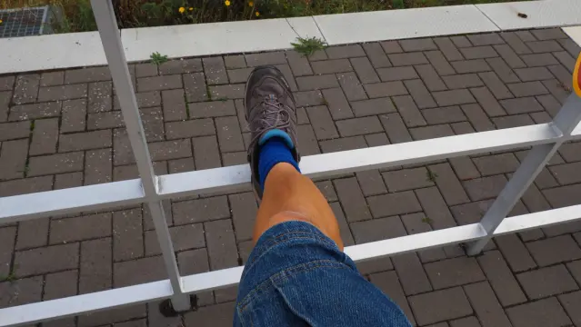 Bein mit einer blauen kurzen Hose , blauem Strumpf und einem grauen Schuh, abgestellt auf einem weißen Geländer.