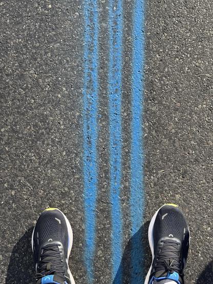 Ein Paar Sportschuhe befindet sich über drei blauen Kreidelinien auf einer Asphaltoberfläche.