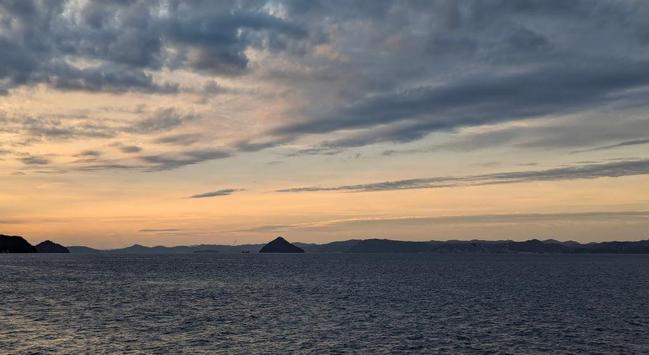 The Seto Inland Sea shortly before dusk. Some islands in the background. The sky is orange, and blue, and grey and white and overall amazing.