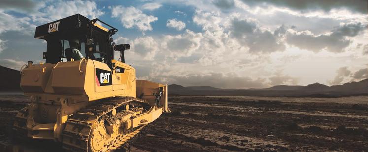 A Caterpillar piece of equipment foregrounded on the edge of a field.