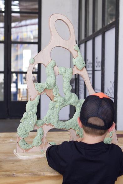 un enfant pose du papier maché vert sur structure bois