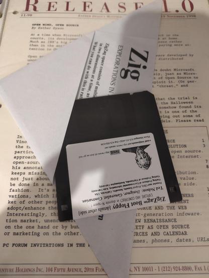 A black 3.5-inch diskette with a white label.  the label advertises it as a "ZigZag™ Boot Floppy" inviting the users to "EXPLORE AND CONSTRUCT in discrete N-space!"

It is gently tucked into a US-letter piece of grey paper on which further instructions have been printed before folding it into a triangular pocket. 

The whole affair is sitting atop a 19 November 1998 issue of Esther Dyson's "Release 1.0" newsletter, with the topic "Open Mind, Open Source"