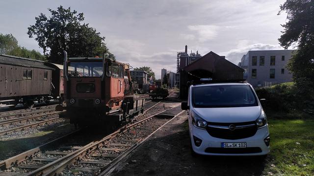 Gleicher Standpunkt, jetzt der Blick Richtung Lokschuppen. Der ist halb verdeckt von einem weißen Lieferwagen. Der Skl hat die Weiche gerade befahren und rangiert an seinen Beiwagen. Der ist mit Aushub beladen, ich glaube Schlacke.