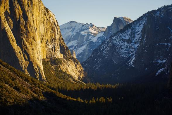 A breathtaking view of a valley with towering cliffs and snow-capped mountains illuminated by the setting sun.