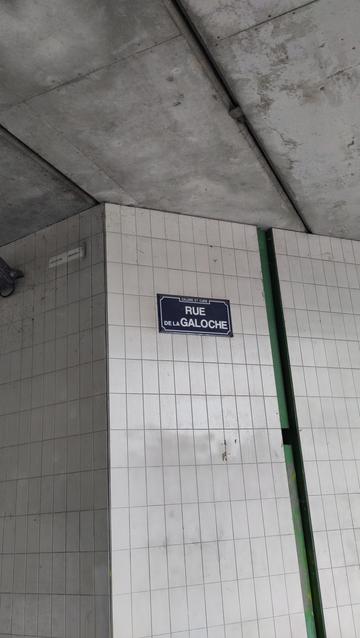 Sur un mur en carreaux de céramique blanche sous un pont, une plaque de rue bleu écrite en blanc indique :"rue de la Galoche"