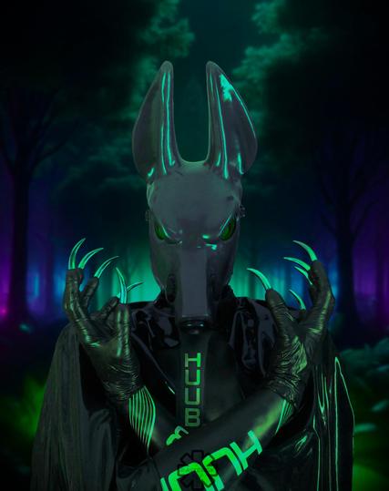 A rubbery black Jackal stands before you, arms crossed exposing his shiny claws in all their glory. In the background, the darkened night forest is lit with green, blue and slightly out of view, purple lights. His shiny body is reflecting colours from the night sky and the green from the lights in front of him.