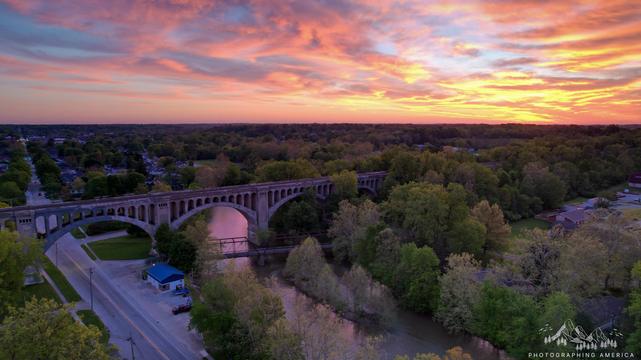 A view from a drone of a sunrise with a cement railroad bridge spanning a river in the foreground.