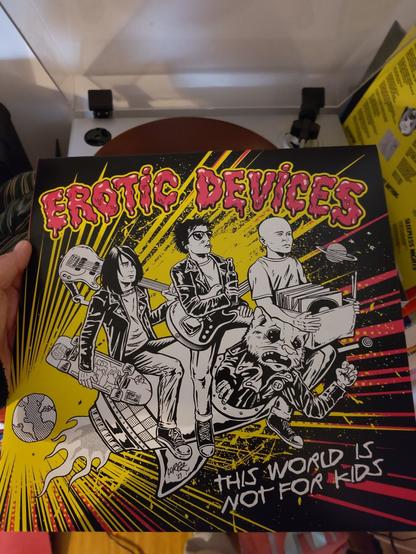 cover of the erotic devices. the band sits on a rocket n comic style, flying away from the Earth