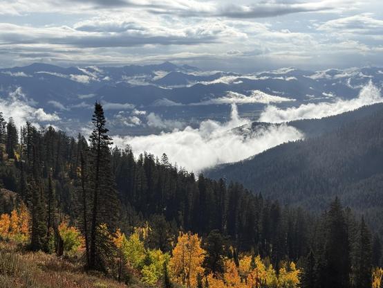 Mountain landscape with colorful autumn trees in the foreground, layered mountains in the background, and clouds in the sky.