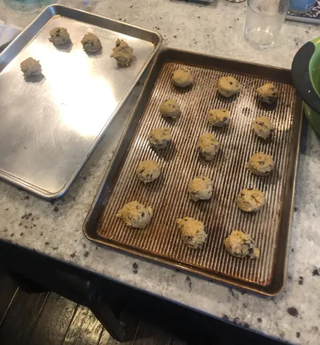 a picture of two baking sheets with 15 cookie batter balls on one and 4 on the other. the sheets are sitting on the counter