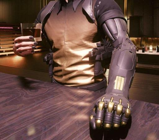 A man with a cybernetic black and golden arm is at a bar counter. In his other hand, which is real, is a glass of whisky. His fingernails are painted black. He's wearing gun holsters on his ribs and his expensive shirt is also black on the shoulders, at the collar, and golden everywhere else. It's tucked into dark trousers.
