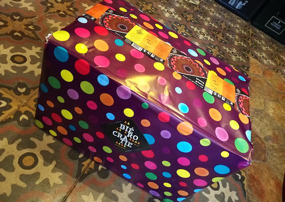 Carton de 24 bouteilles emballé dans un papier cadeau avec des étiquettes de bières utilisés comme scotch au dessus et un sticker Biérocratie sur le devant.