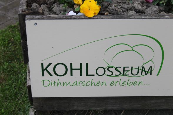 Foto mit Text auf einer Tafel:
"Kohlosseum 
Dithmarschen erleben"