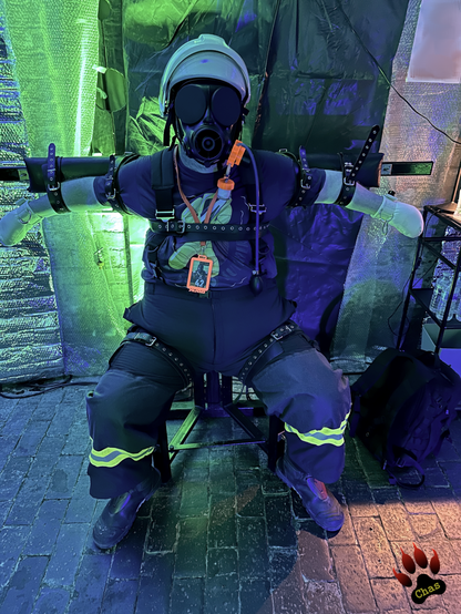 human pup, wearing firefighter trousers, t-shirt, Haix boots, helmet and padded mitts sitting on a bondage chair with it's legs apart, arms spread out and bound horizontally