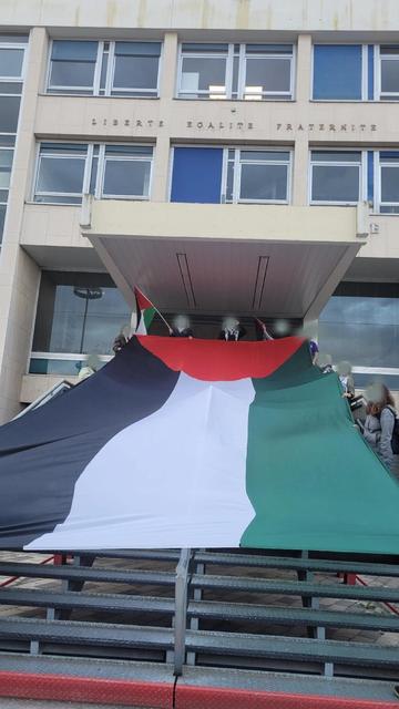une 12aine de personnes aux visages floutés tendent un drapeau d'environ 10 m de long sur les escaliers de la mairie de Sotteville-les-Rouen