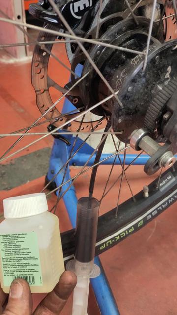 Gros plan sur un moyeu à vitesses de roue de vélo.
Une seringue de purge pend du moyeu avec un liquide noir, à côté je tiens un flacon d'huile Rohloff neuve où l'huile est claire, presque transparente