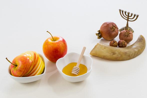 Still life photograph of Rosh Hashanah symbols:  apples, honey, pomegranates, shofar, and menorah; designed by freepix.com