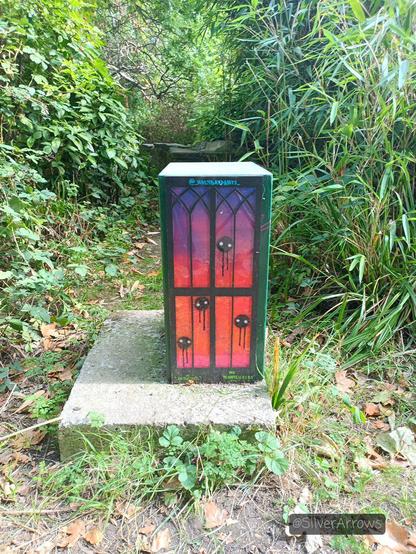 I forget what these boxes are, but someone has put a stained glass window effect art on it. There is a sunset coloured background with black discs with eyes, dripping down