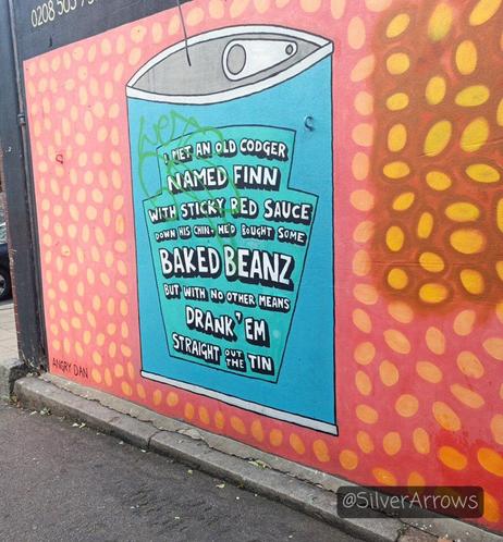 Cartoon style street art. Baked beans background with a turquoise tin of beans with a heinz style label. Poem reads:

I met an old codger called Finn
With sticky red sauce down his chin
He'd bought some baked beanz
But with no other means
Drank em straight out of the tin