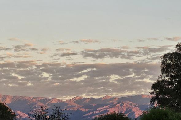 Desert mountains highlighted by newly risen sun - peaks in pink and shadow - with clouds overhead