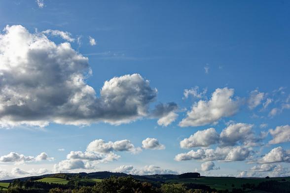 Blauer Himmel mit weißen Wolken. Am unteren Bildrand schmal eine Hügelkette