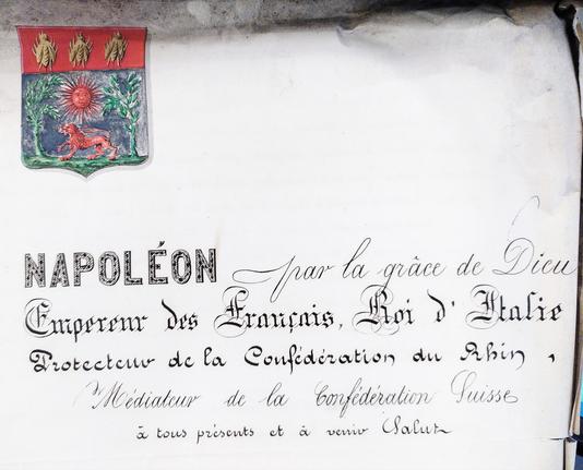 Page d'archives avec des armoiries colorées en haut à gauche (trois abeilles d'or sur fond rouge, un soleil rouge et un lion rouge sur fond vert de végétation et ciel bleu sombre), et un début de texte : Napoléon, par la grâce de Dieu empereur des Français, roi d'Italie, protecteur de la confédération du Rhin, médiateur de la Confédération suisse, à tous présents et à venir, salut "