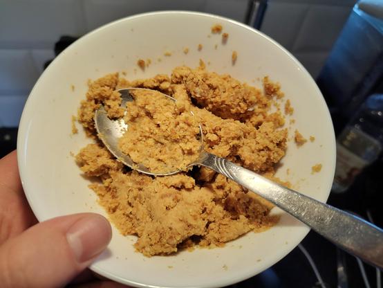 A white bowl filled with what could be best described as course light colored peanutbutter, a spoon half filled with the stuff stuck into the bowl