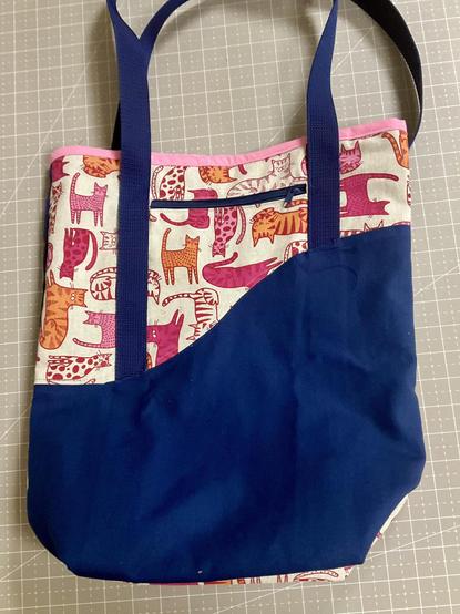 Eine Tasche aus Stoff liegt auf einer Taupefarbenen Schneidematte. 
Die Fasche ist blau und Beige/pink-gemustert und hat blaue Griffe aus Gurtband