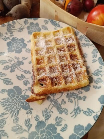 A lone Belgian waffle on a plate, sprinkled with powdered sugar.