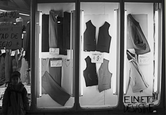 Fotografía en blanco y negro de un niño delante de una tienda antigua de ropa.