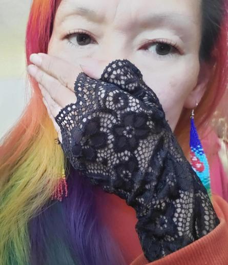 Asian woman with multi-colored hair covering mouth with hand wearing a black lace glove, and beaded earrings.