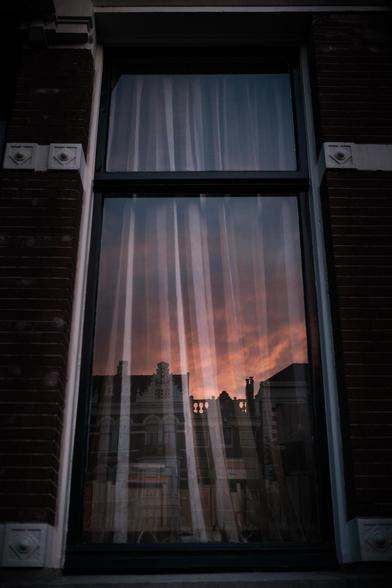 A reflection in a window. The reflection shows the sunset and a house in Amsterdam.