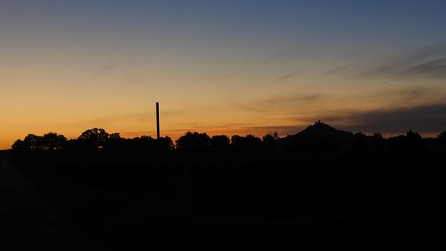 Orangeblauer Himmel im Hintergrund der Schattenriss eines Vulkankegels mit Burg