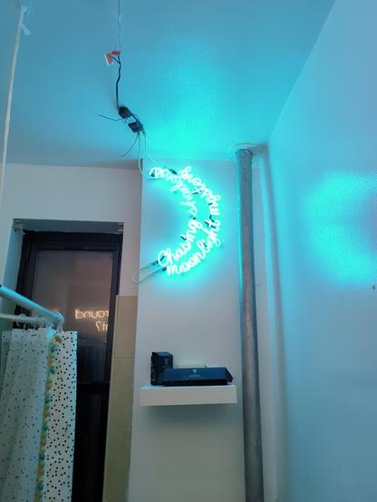 The turquoise blue moon seen zoomed out in the bathroom. The neon is so bright it is blowing out the image. Shower curtain seen to the left.