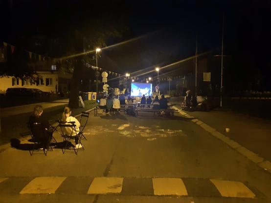 An improvised open-air cinema in one of Prague's streets, with about a dozen people watching a film.