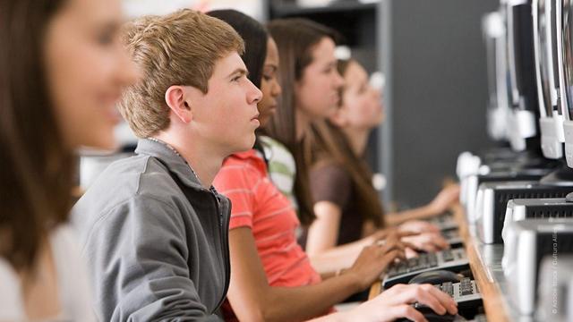 Students in a school sitting in a row on computers, typing something and looking concentrated at the screen.