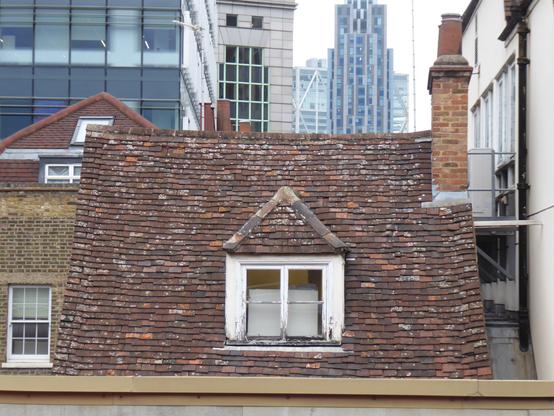 An old red-tiled roof at the rear of a building in central London. The tiles are sagging and covered in lichen.

A dormer window with a white frame faces the viewer. The window frame is peeling rotten.