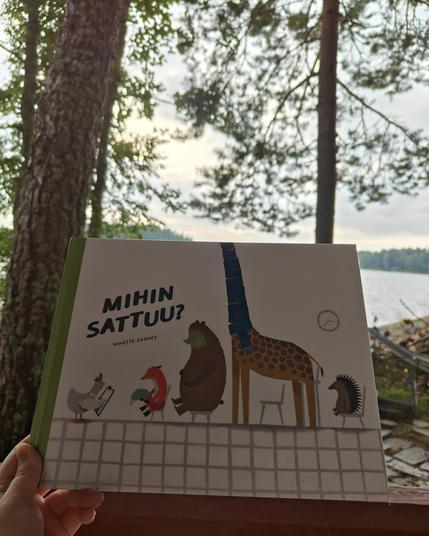 Kuvassa Mihin sattuu? -kirja kuvattuna vasten järveä. Sivuilla näkyy hieman kalliota ja mäntyjä.