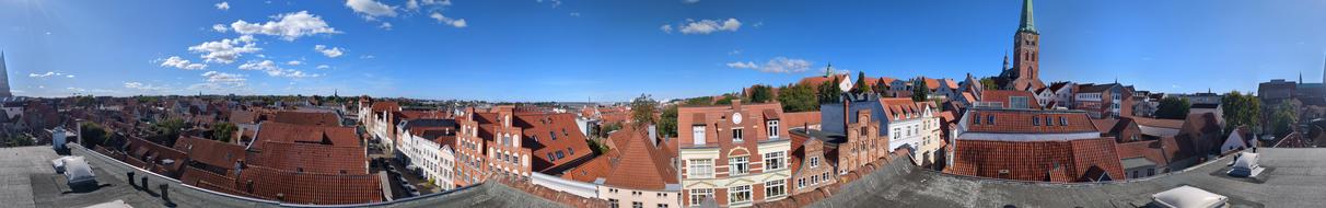 Eine rundum Panoramaaufnahme von einem Dach in der Innenstadt. Rote Ziegeldächer, historische Fassaden, Kirchturm, roter Backstein, strahlend blauer Himmel