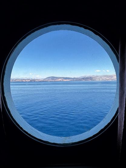 View of the sea and of the island of Corfu from a porthole on a ferry.