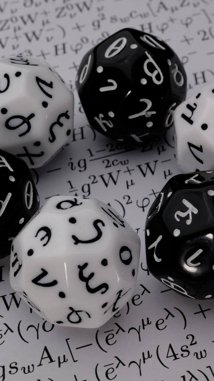 Dice with greek letters on the faces, on a sheet of paper with a very long equation on it.