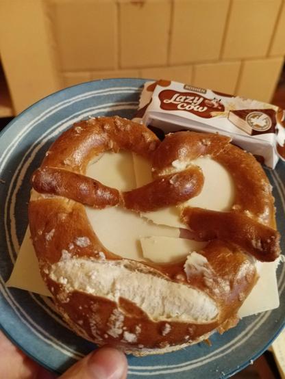 A Brezel (I refuse to spell it "pretzel") with butter, cheese and ham sausage (under the cheese) on a small plate. Also on the plate a packaged Ukrainian snack labeled "Lazy Cow".