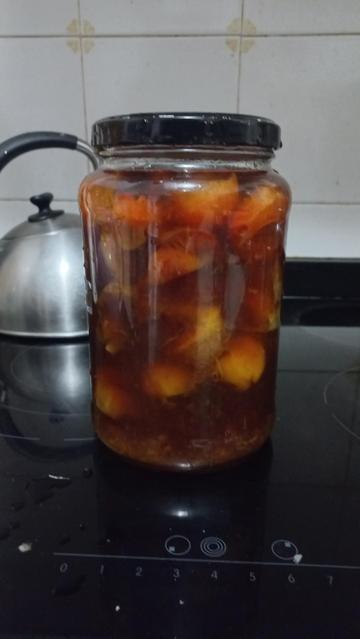 Un tarro de cristal grande con líquido dorado y trozos de fruta.