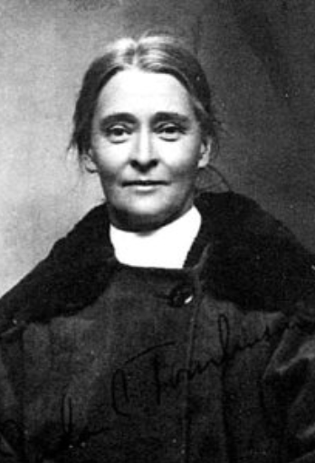 Sada C. Tomlinson, from a 1925 passport application; a smiling white woman of middle age, wearing a dark coat; her greying hair is parted and dressed to the nape