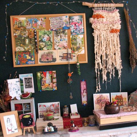 Photo of my Autumn equinox altar with a bulletinboard filled with postcards, a woven wall hanging, a few spell jars and boxes, a granny square cauldron, and other trinkets and cards that remind me of Autumn and home.