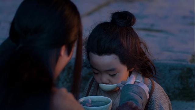 Close in shot over an out of focus Wen Ning's right shoulder to where A-Yuan is shown eating from a spoon held by Wen Ning over a bowl containing lotus and pork rib soup.