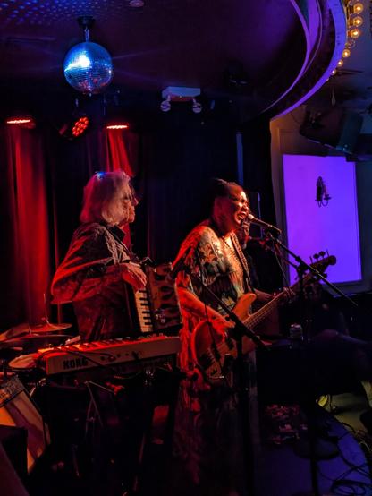 A photo of FaithNYC performing at Berlin in New York City. The photo is shot from the side, and includes singer/bassist Felice Rosser with the band's keyboardist who is doubling on accordion.