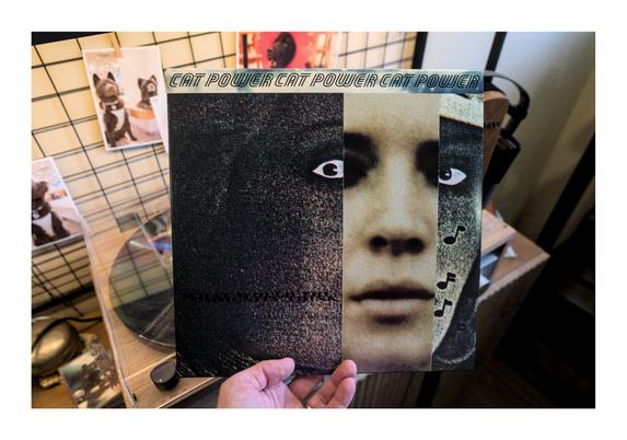 Photo of the vinyl release of Cat Power's "What Would The Community Think" album held up in front of my record player, which can be partially seen in the background, along with some photos hanging on the wall of our doggo.