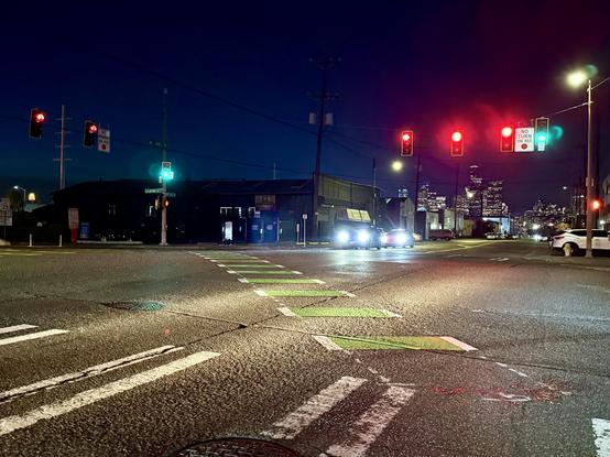 The intersection of 6th Avenue and Lander Street at night with diagonal crossbike markings and green bicycle signals